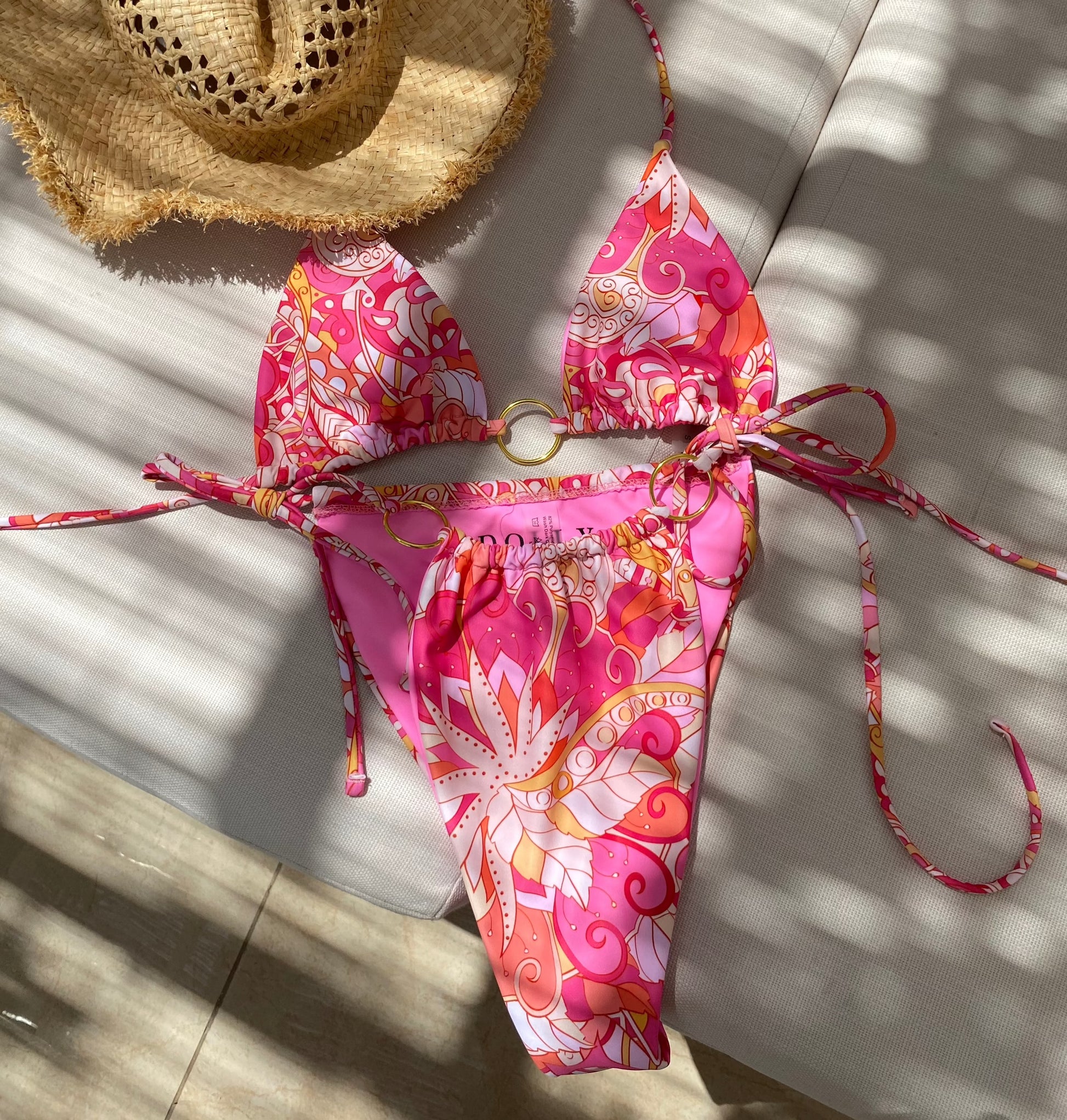 Beautiful vibrant pink printed bikini bottoms with tie side and gold o-ring detail - flat lay